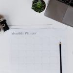 A stylish desk setup featuring a camera, laptop, and monthly planner, perfect for planning and productivity.