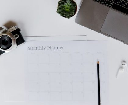 A stylish desk setup featuring a camera, laptop, and monthly planner, perfect for planning and productivity.