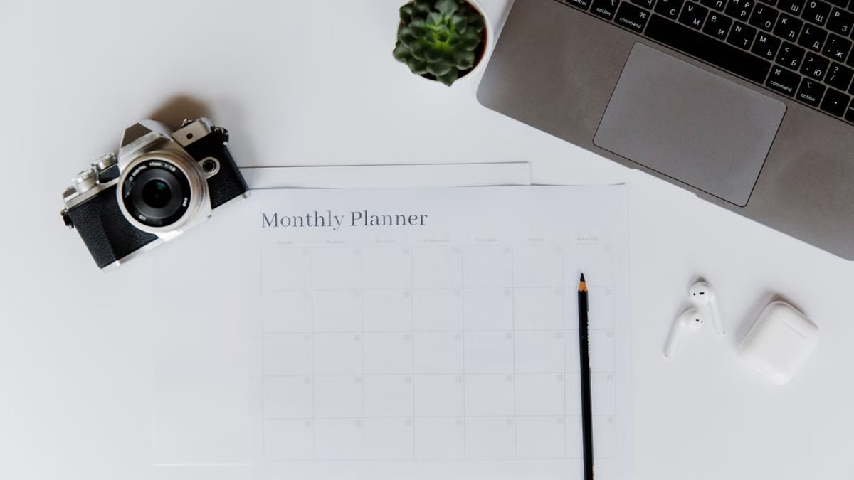 A stylish desk setup featuring a camera, laptop, and monthly planner, perfect for planning and productivity.